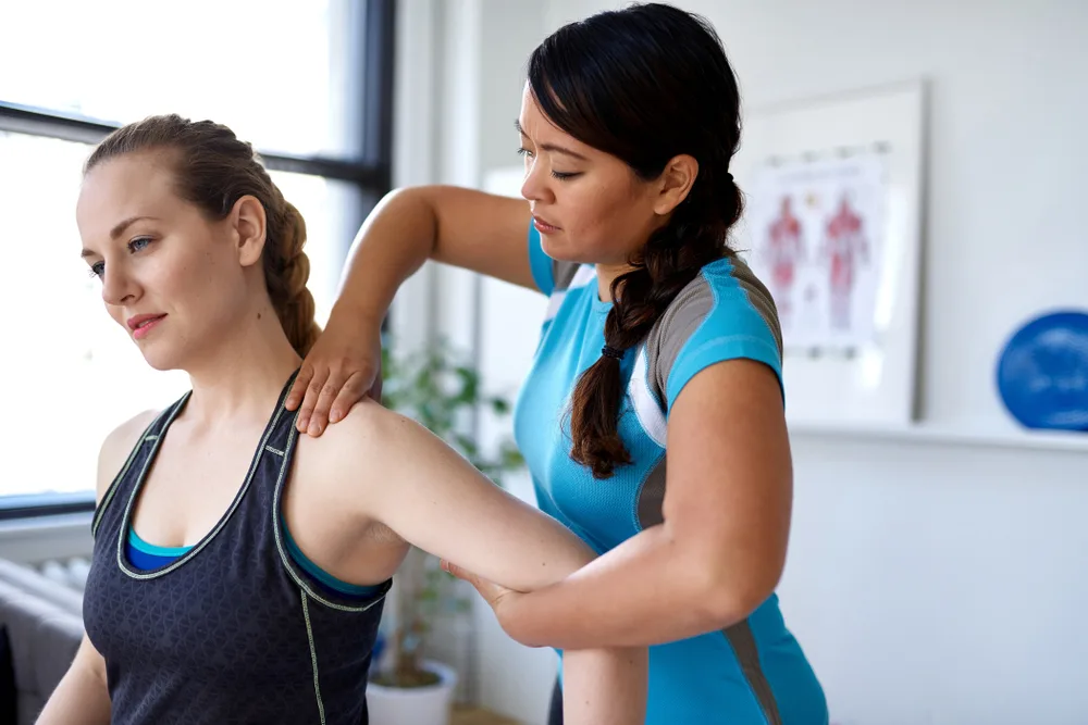 Therapist working on the shoulder of a woman in athletic clothing