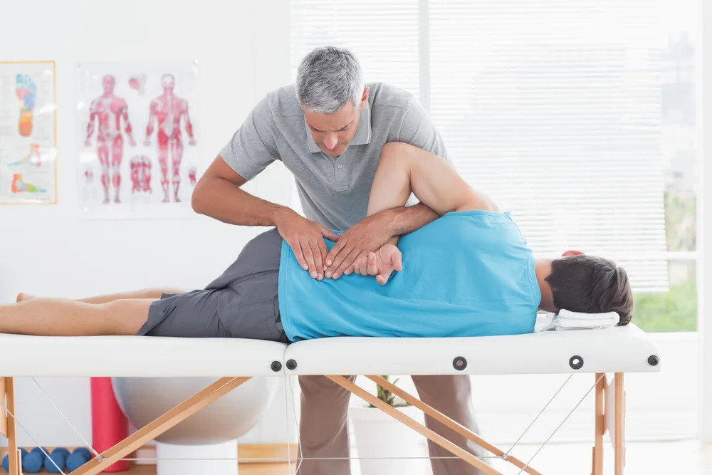 Therapist adjusting the back of an older man lying on a treatment table