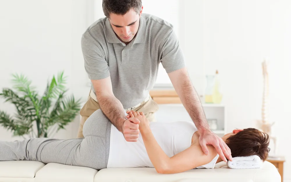 Therapist stretching the arm of a woman lying on a treatment table