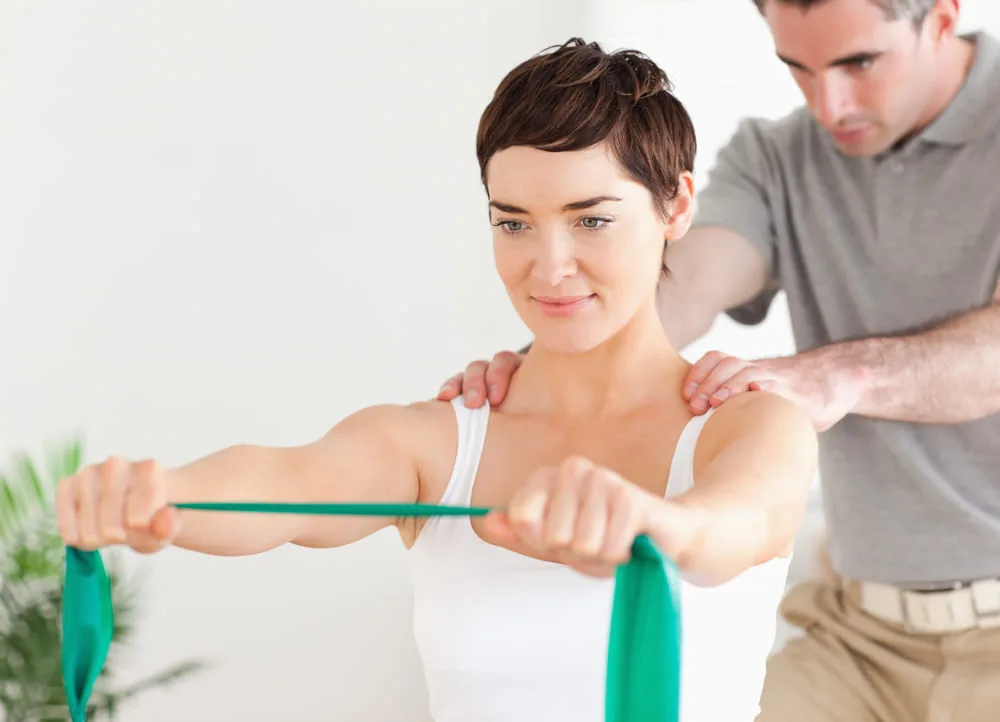 Therapist supporting a woman's shoulders as she pulls a resistance band