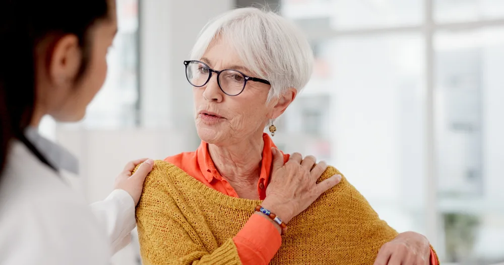 Older woman seated while a clinician's hands rest on her shoulders