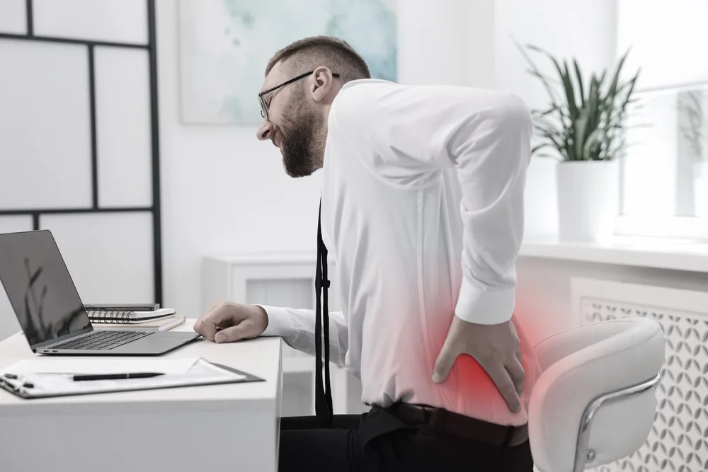 Man bent over a laptop at a desk, with a red glow over his lower spine