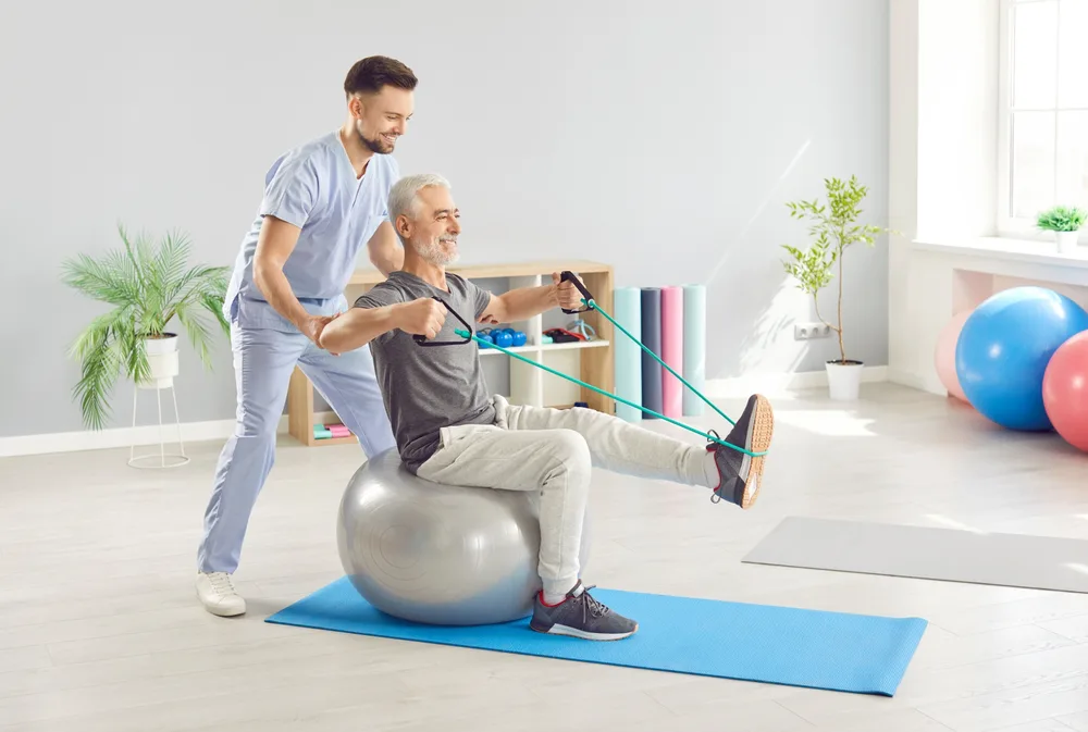 Therapist guiding an older man through an exercise on a stability ball