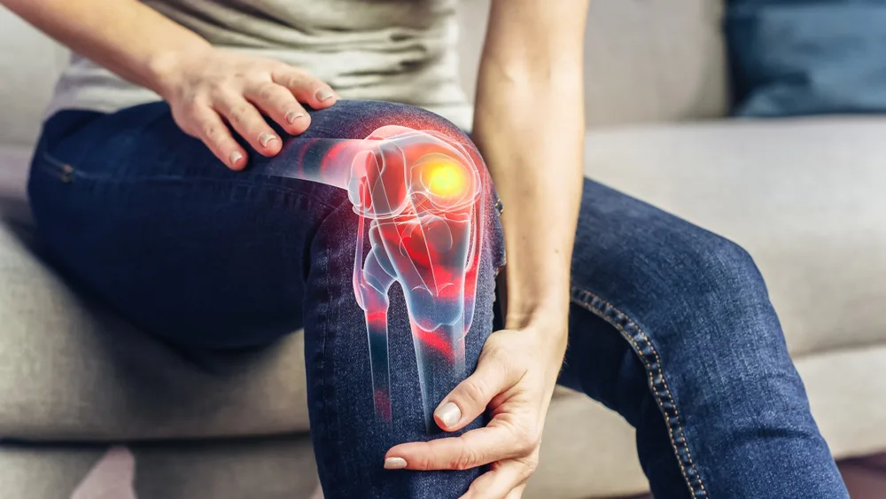 Knee held in both hands with a glowing overlay of the joint beneath
