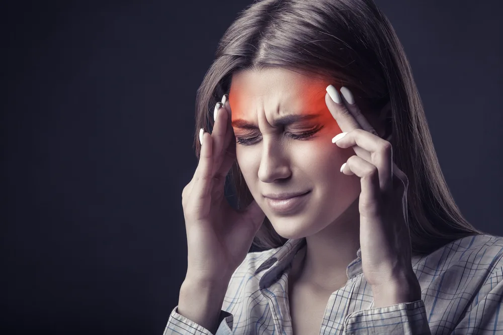 Woman pressing both temples, with a red glow marking a headache