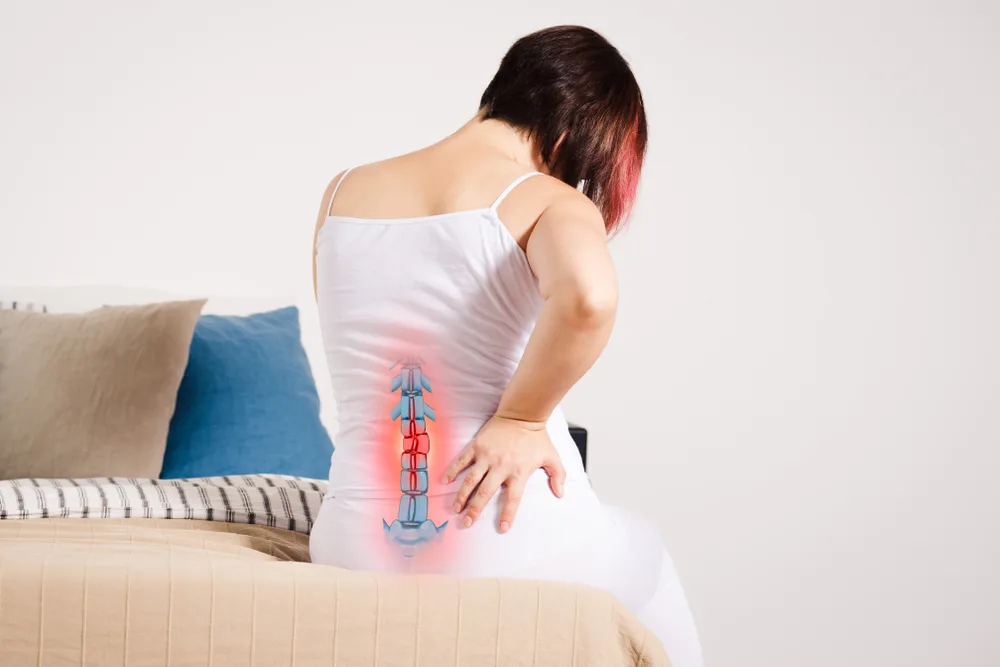 Woman seated on a bed with a glowing overlay along her spine and sciatic nerve