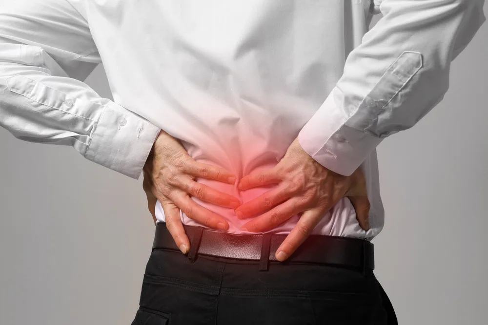 Person in a white shirt pressing their lower back, with a red glow marking pain