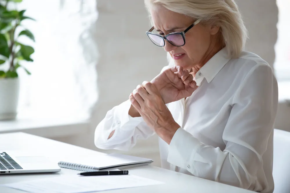 Older woman at a desk rubbing a sore hand