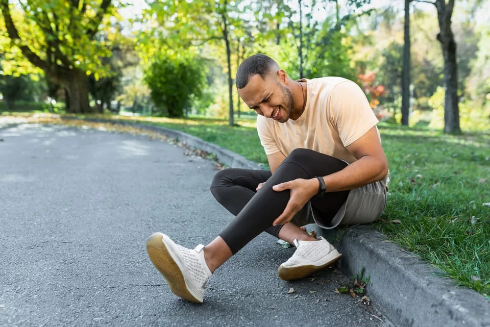 Man sitting on a path outdoors holding his lower leg