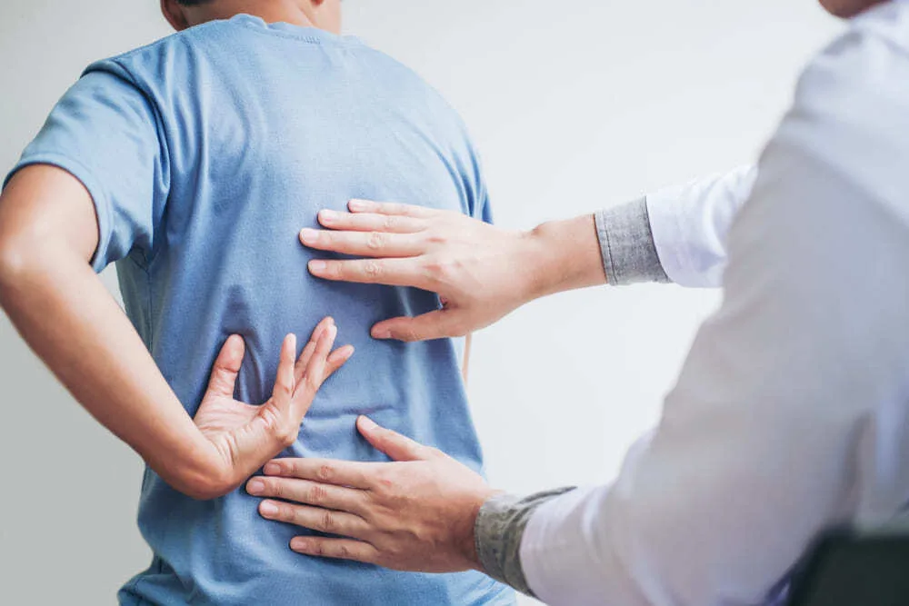 Clinician's hands reaching towards a man's lower back