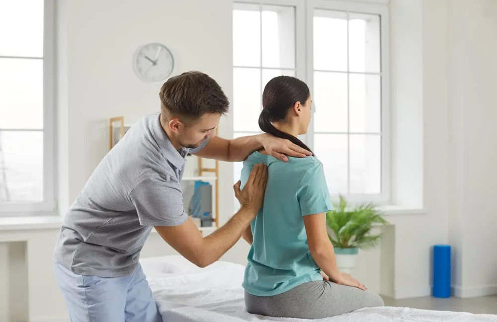 Therapist correcting the posture of a standing woman in a treatment room