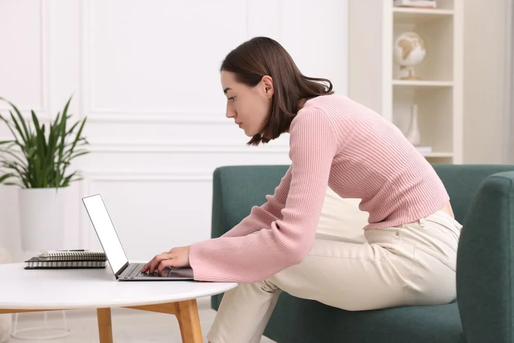 Woman slouching at a laptop while holding the back of her neck