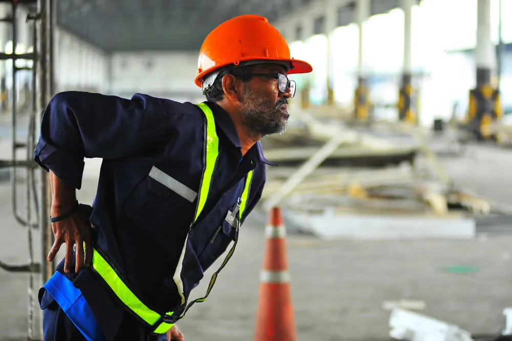 Construction worker in an orange helmet holding his shoulder at a building site