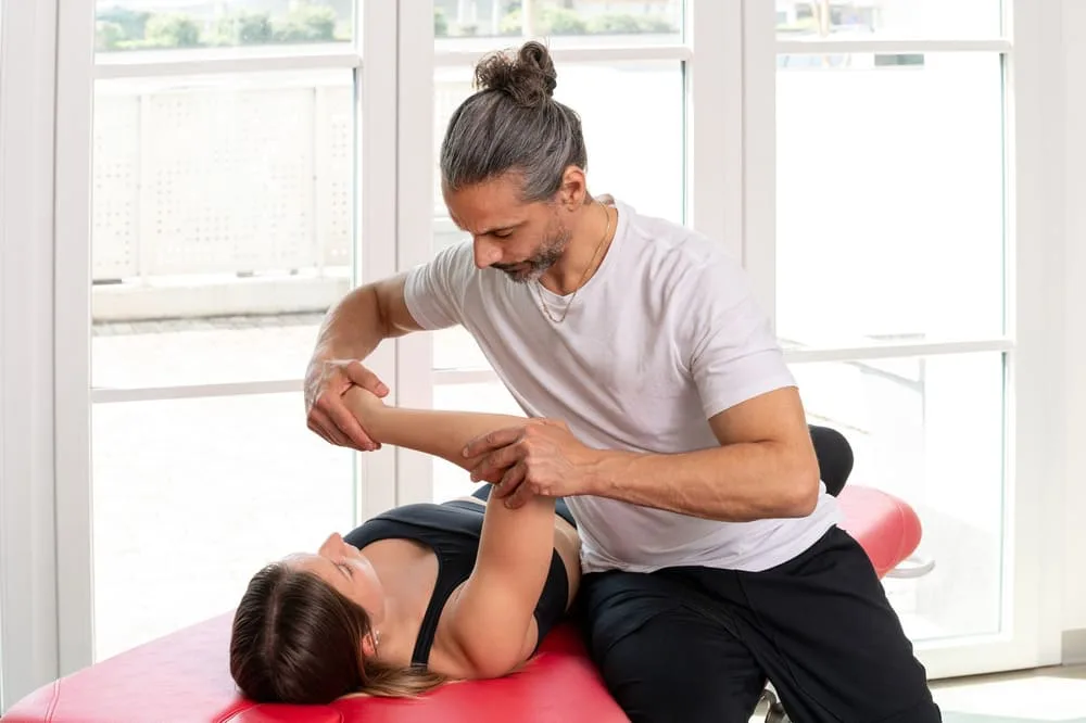 Therapist stretching a woman's arm and shoulder as she lies on a mat