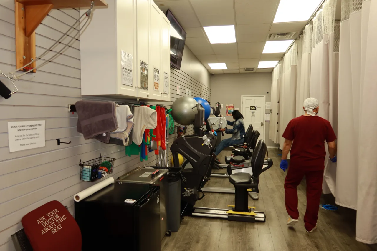 Cardio machines along a slatwall of resistance bands, with the treatment bays beyond
