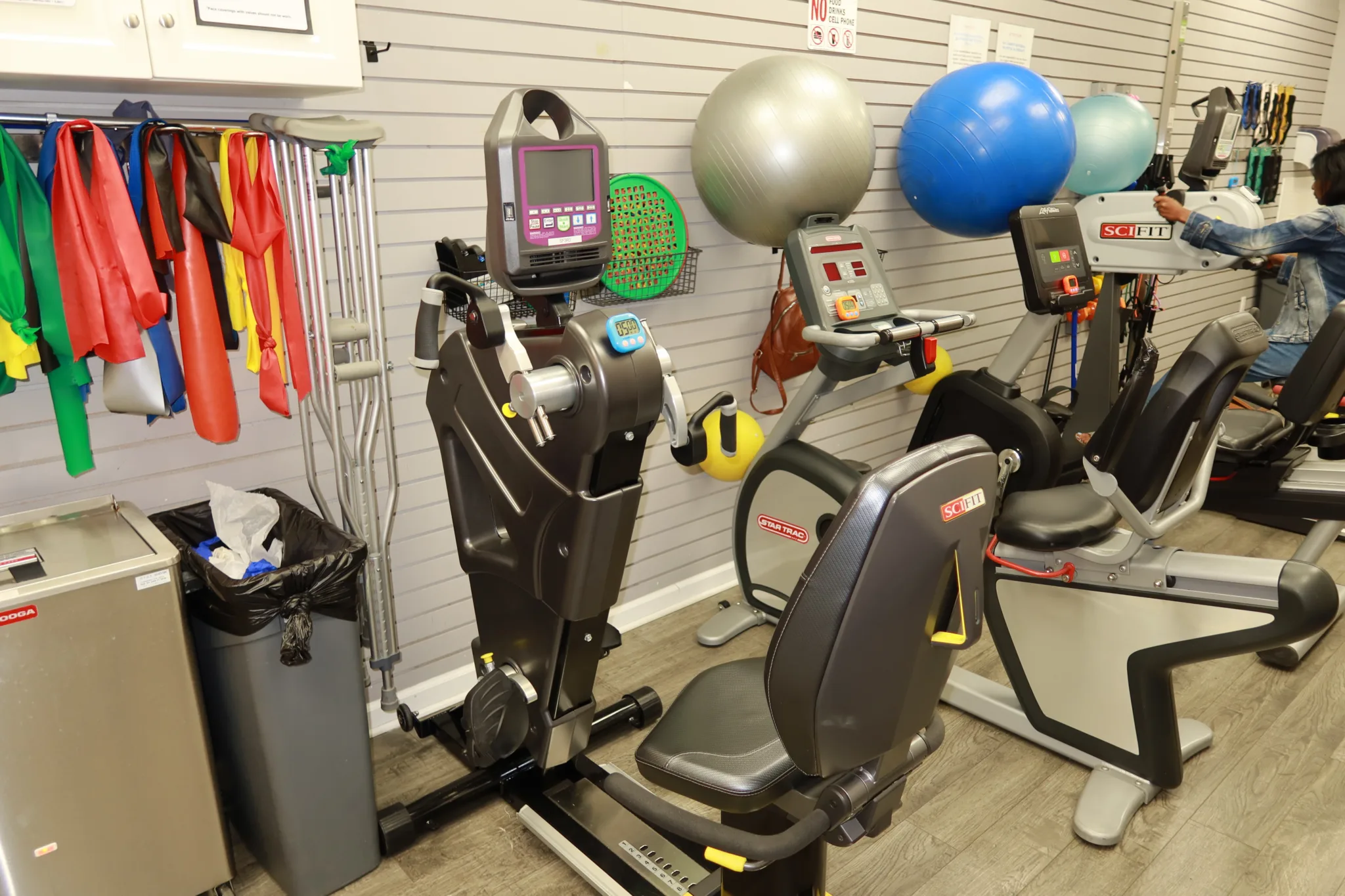 Cardio machines and exercise balls against a slatwall hung with resistance bands