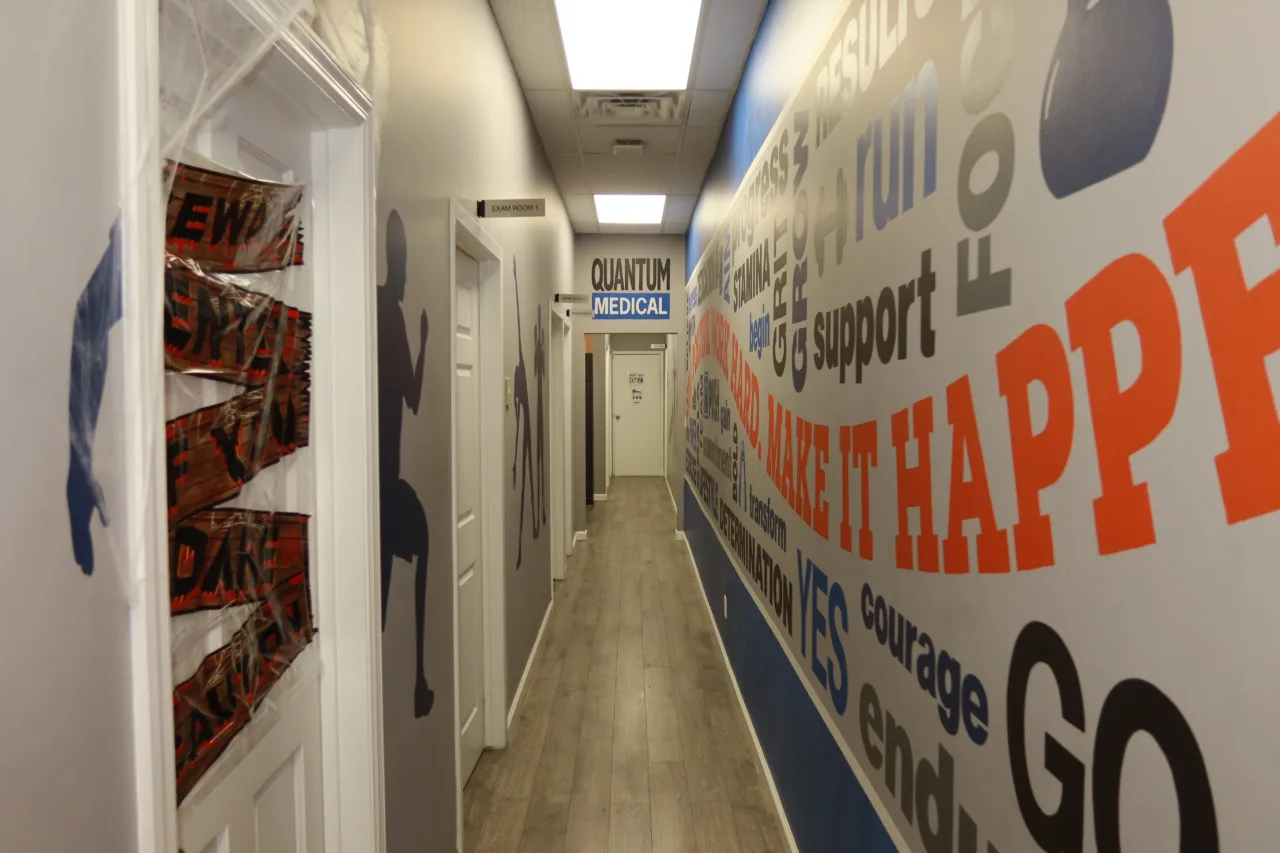 Corridor to the treatment rooms, lined with a motivational mural and the branded sign at the far end