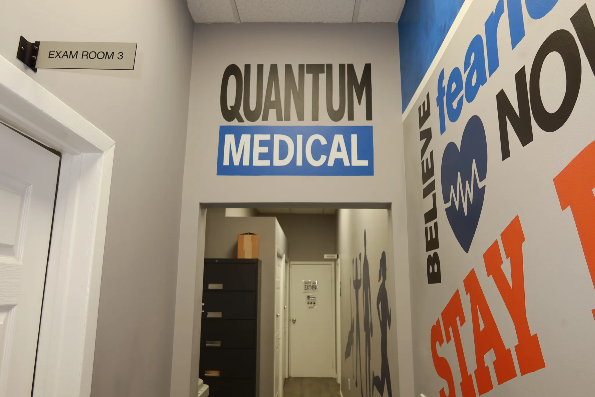 Branded wall sign above the passage to Exam Room 3, beside a motivational mural