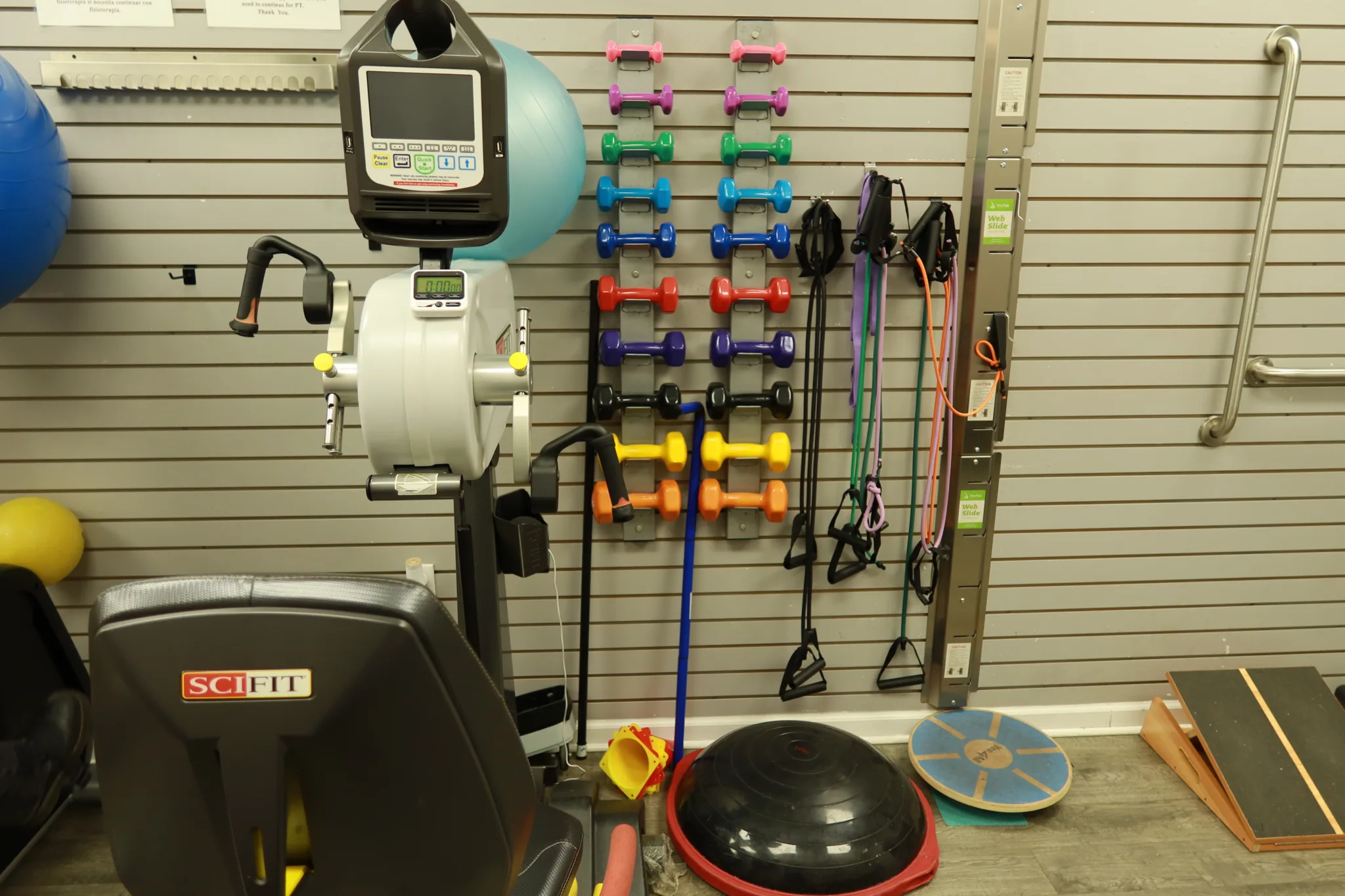 Equipment wall with racks of hand weights and resistance bands, an upper body ergometer and balance trainers