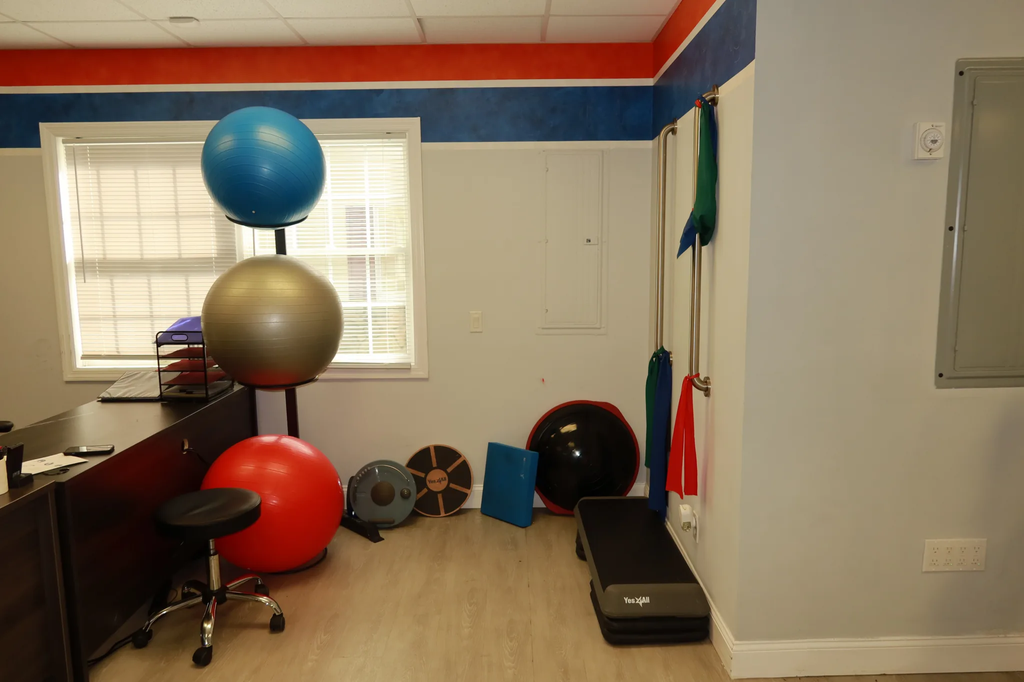 Corner with stacked exercise balls, weighted discs, a step platform and resistance bands on the wall