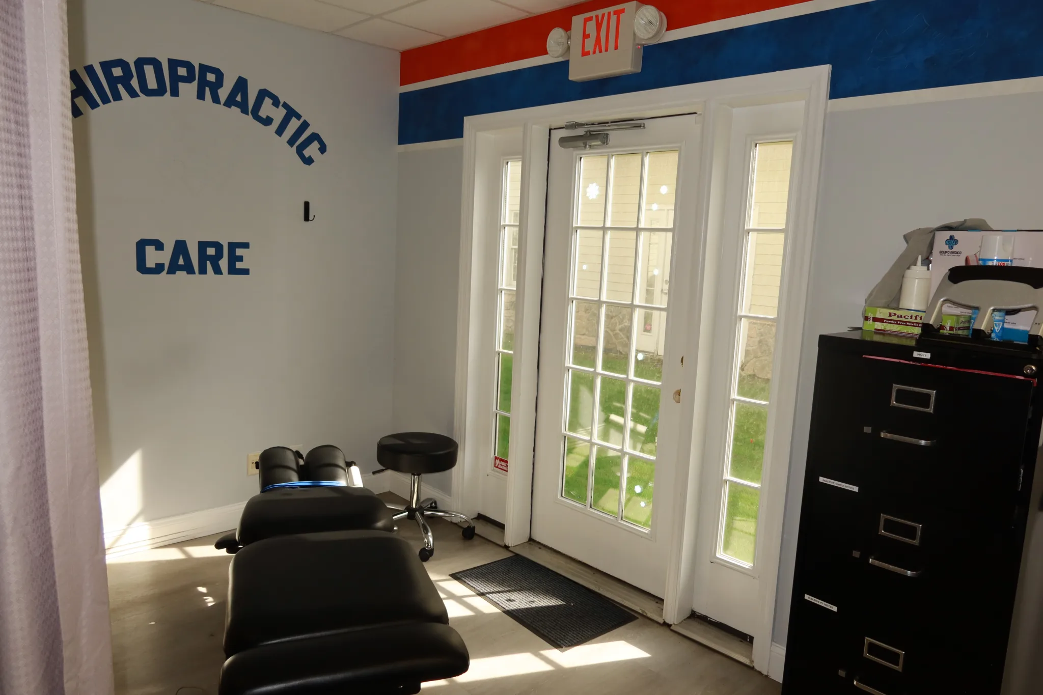 Chiropractic adjustment table by the entrance doors, under Chiropractic Care lettering on the wall