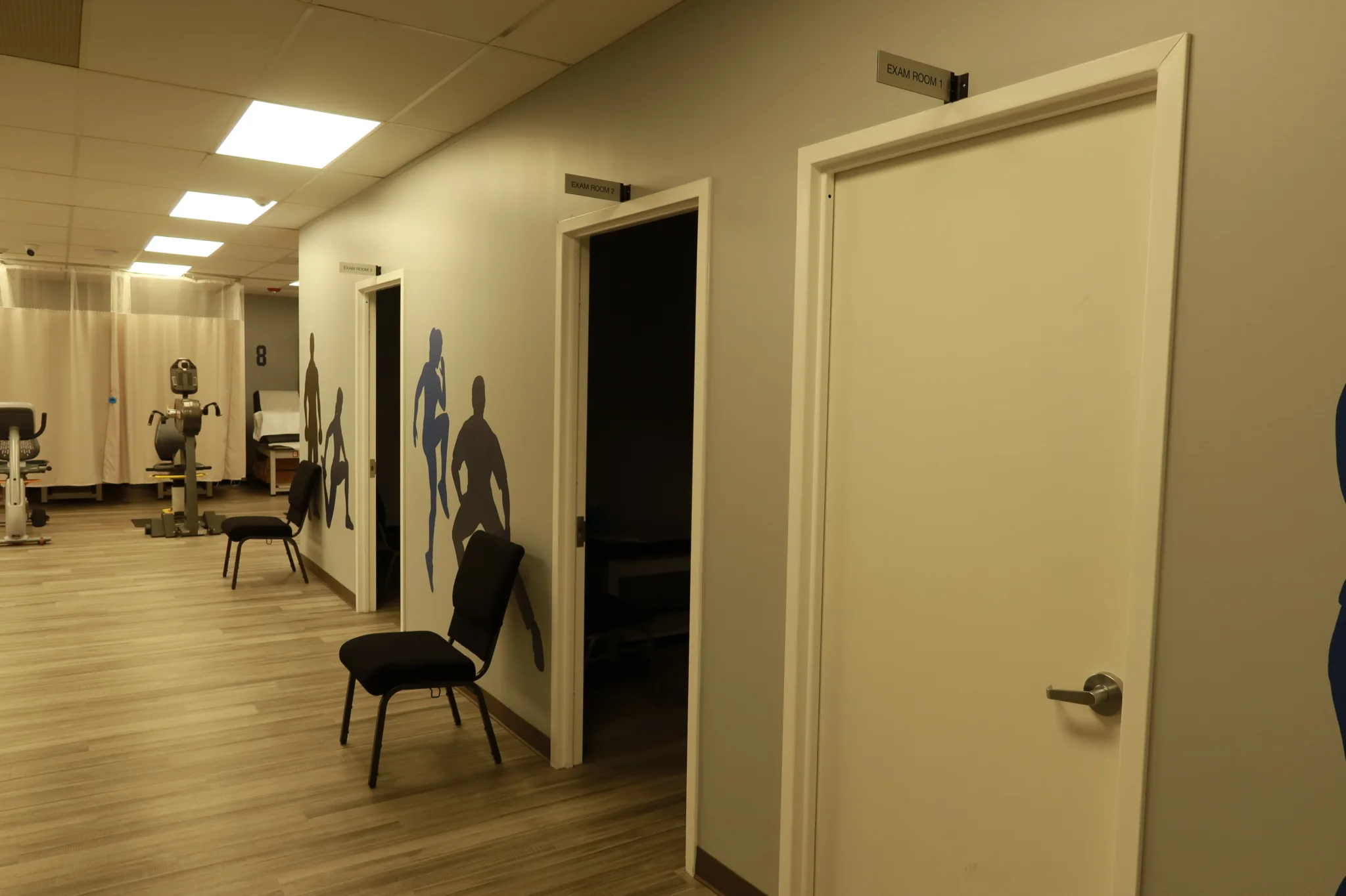Hallway to the treatment rooms, with athlete silhouettes on the wall and the exercise floor beyond