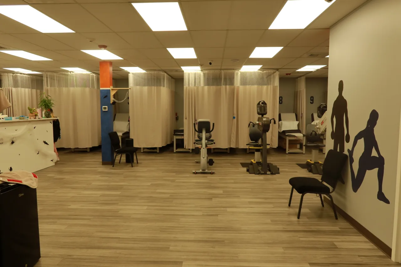 Open exercise floor with curtained treatment bays, cardio machines and athlete silhouettes painted on the walls