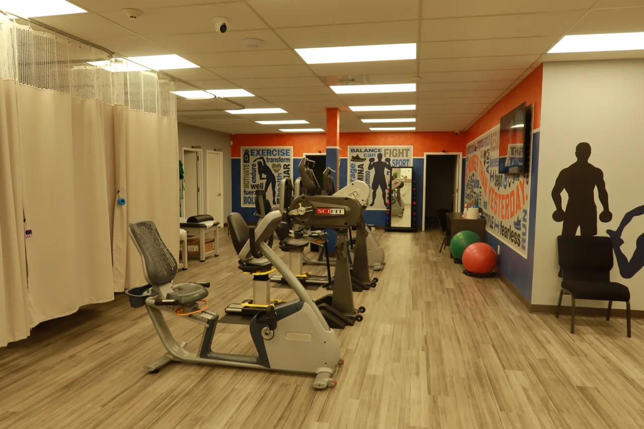 Cardio machines on the exercise floor, with curtained treatment bays on one side and motivational murals on the other