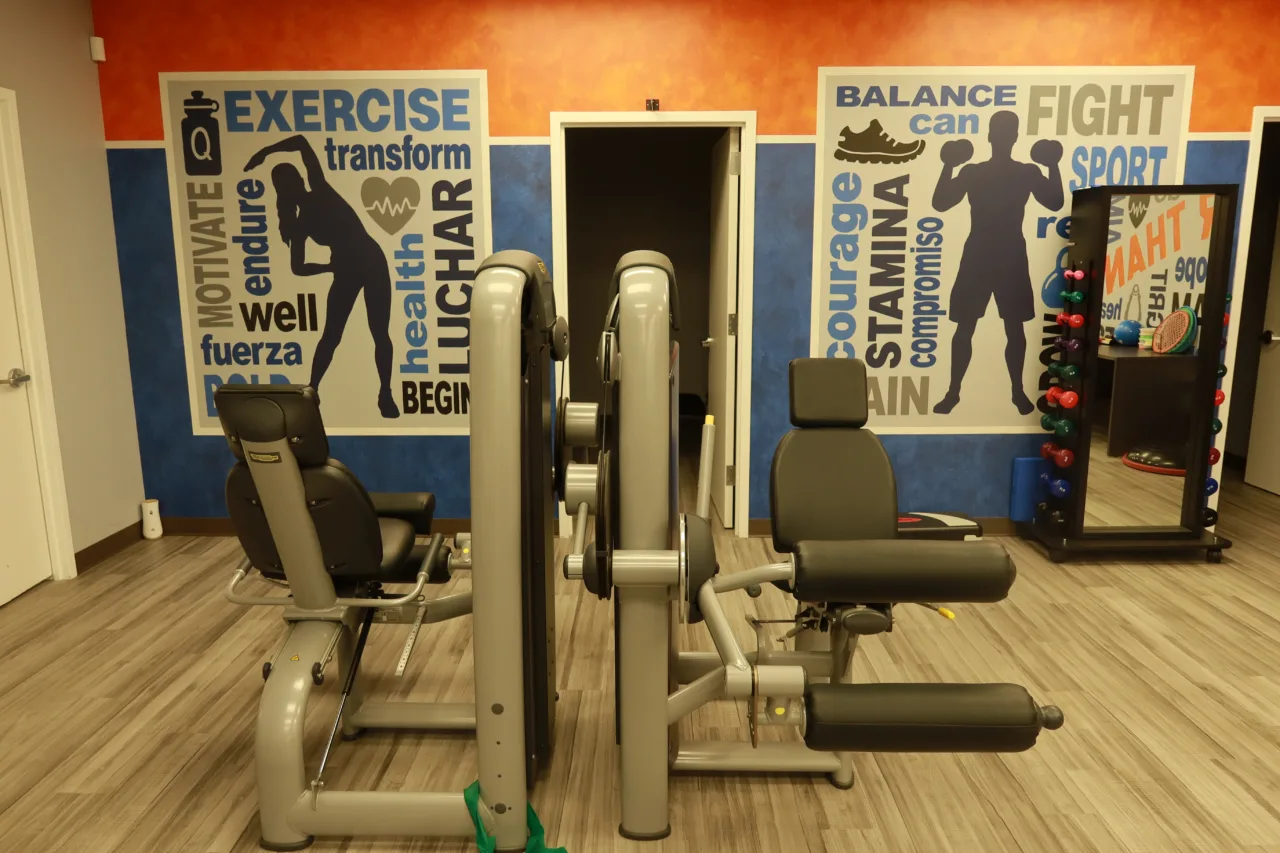 Resistance training machines in front of the motivational murals, with a dumbbell rack and a mirror alongside