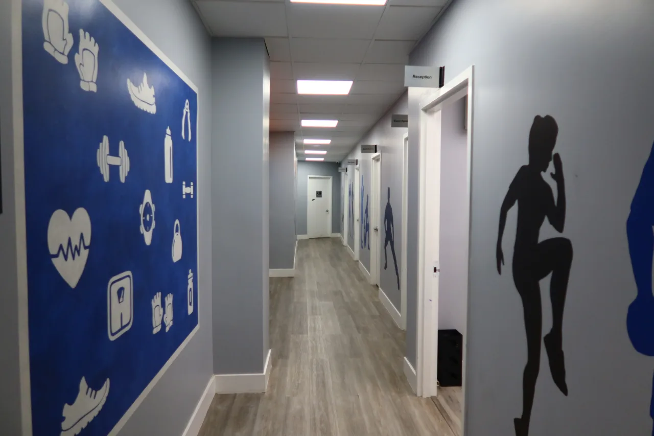 Corridor to the treatment rooms, with a panel of painted health and fitness icons and athlete silhouettes