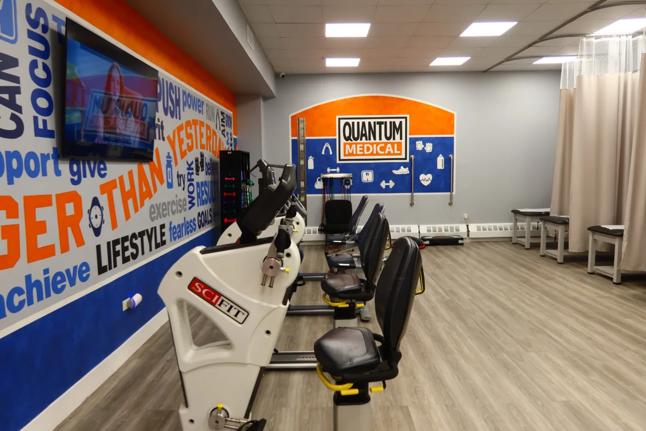 Cardio room with recumbent bikes, a wall-mounted screen and word murals wrapping the walls