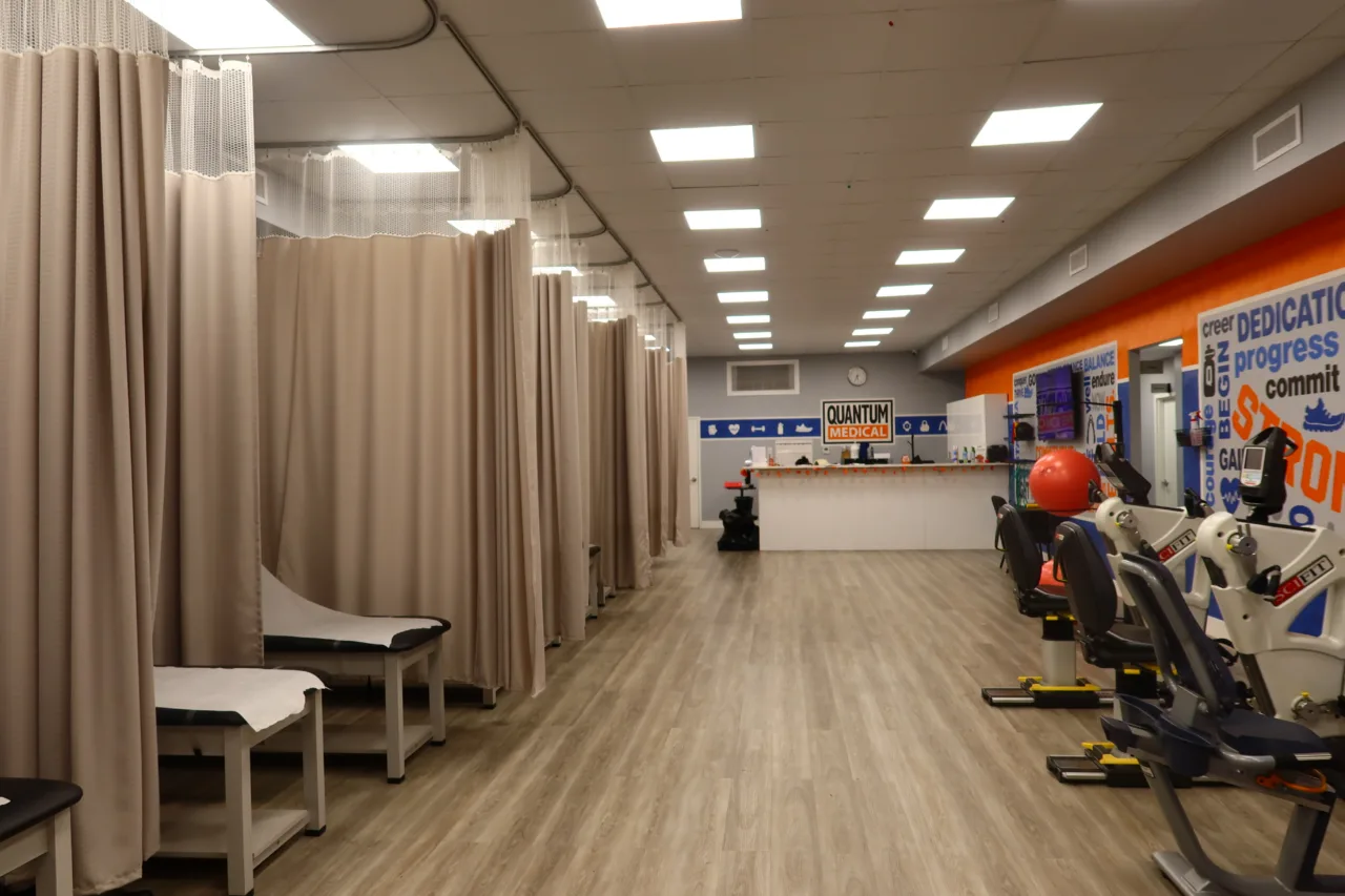 Treatment floor with curtained therapy bays on one side, exercise bikes on the other and the reception desk beyond