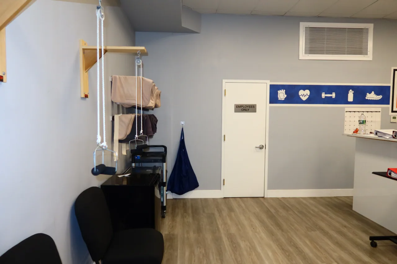 Therapy corner with a wall-mounted pulley system, a supply cart and seating beside a staff door