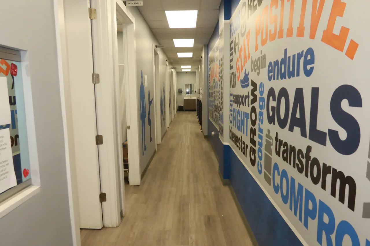 Corridor lined with a bilingual word mural, leading past the treatment rooms