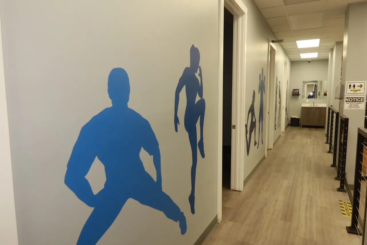 Corridor of treatment rooms with blue athlete silhouettes painted along the wall