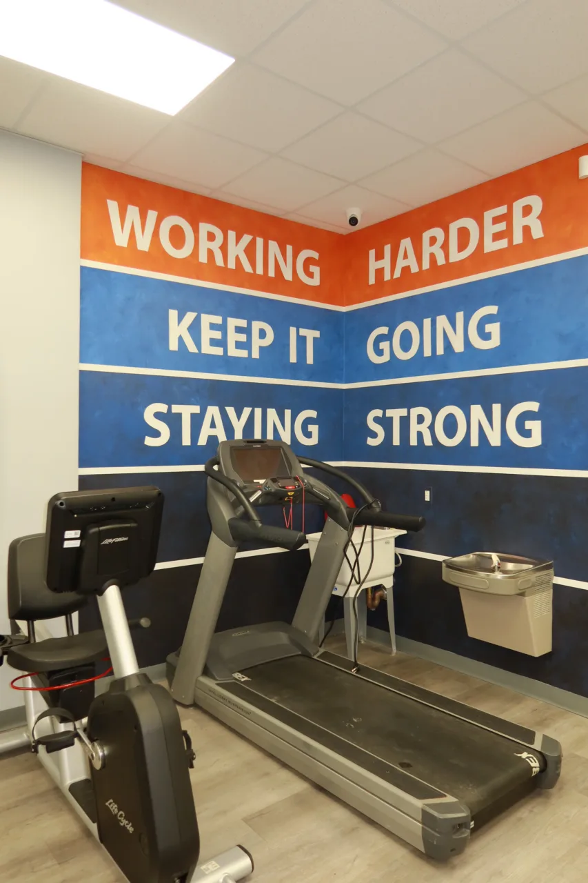 Treadmill in front of a mural reading Working Harder, Keep It Going, Staying Strong
