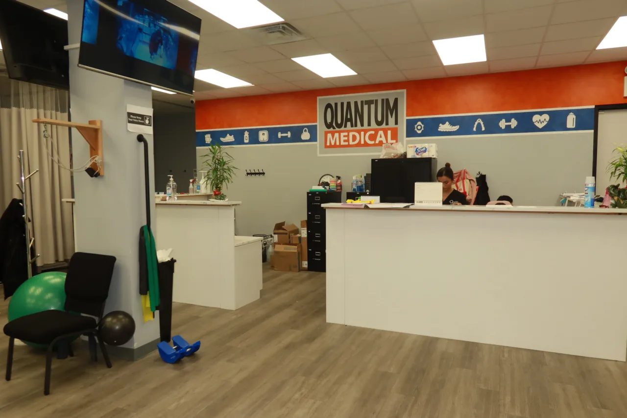 Reception desk under the branded wall sign, with a wall-mounted screen and therapy equipment nearby
