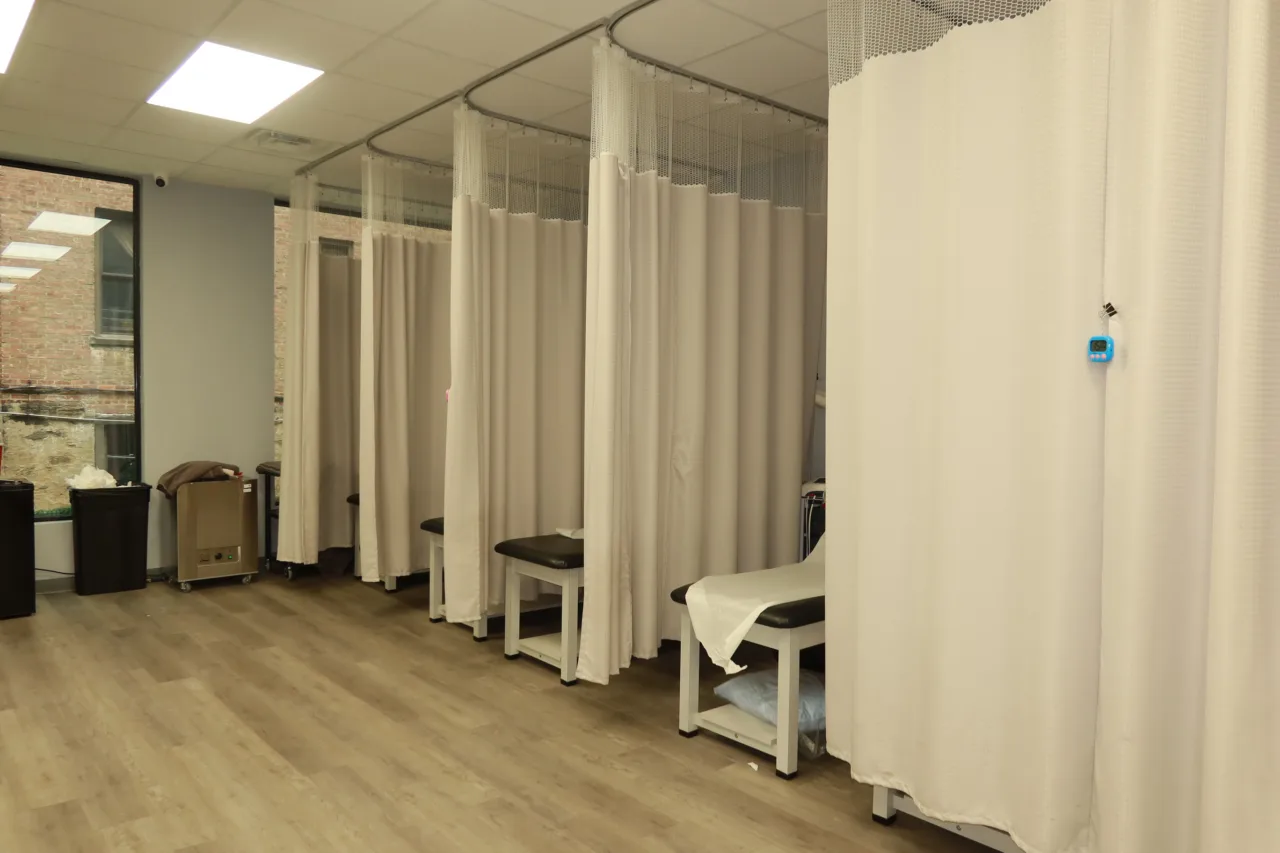 Row of curtained treatment bays with therapy tables, lit by the street windows