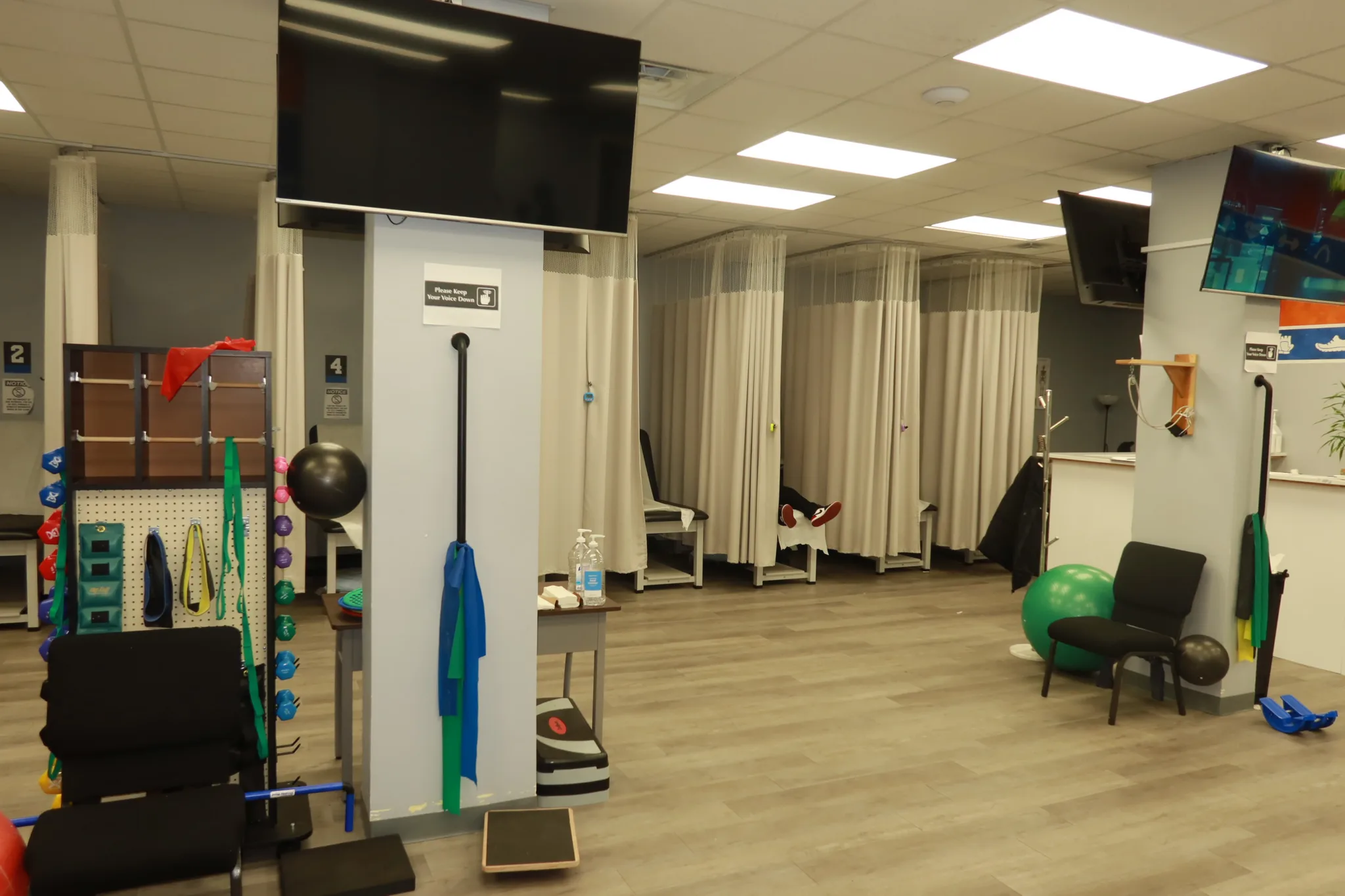 Numbered treatment bays around the exercise floor, with a pegboard of resistance bands and a wall-mounted screen