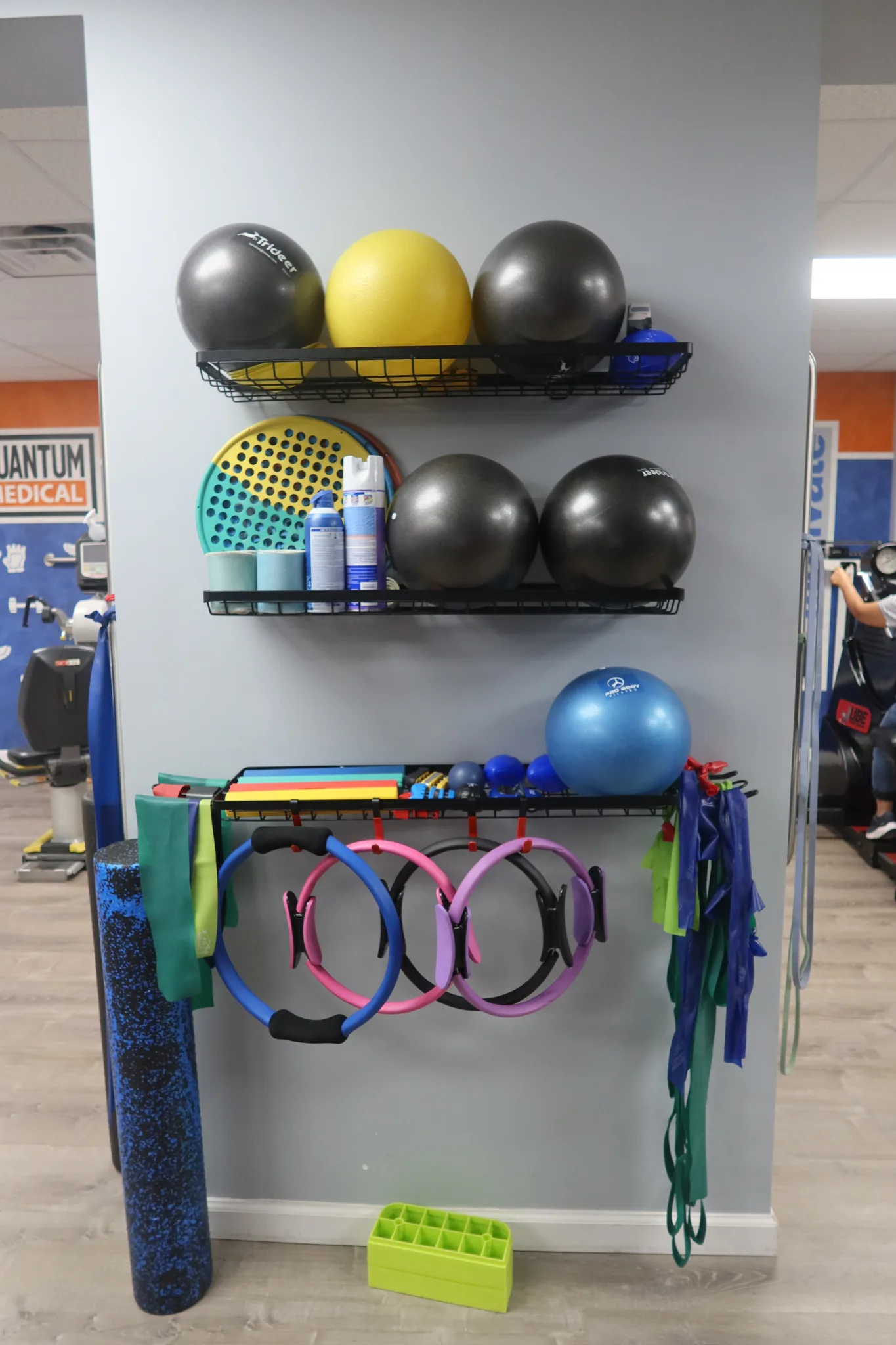 Wall shelves of exercise balls and balance discs above a row of Pilates rings and resistance bands, with a foam roller alongside