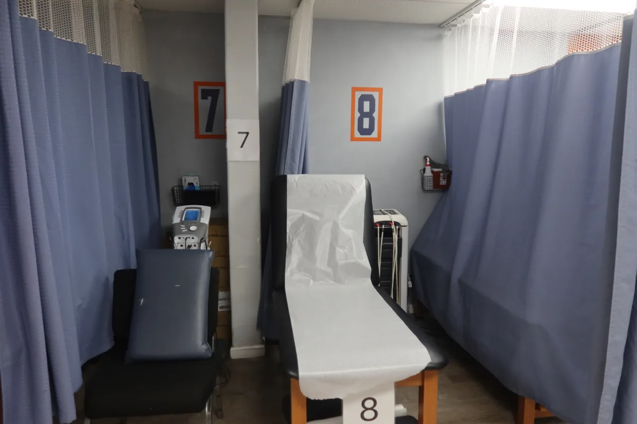 Numbered treatment bays seven and eight between privacy curtains, with a therapy table, a chair and an electrotherapy unit