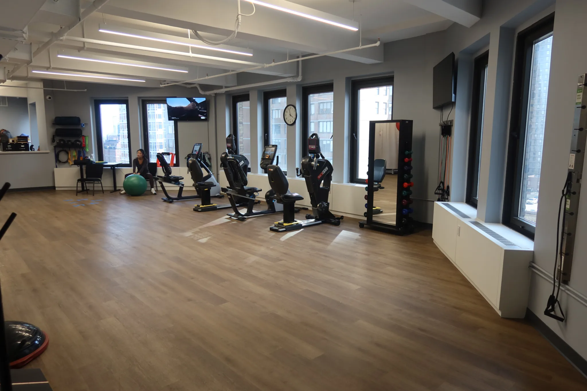 Open exercise floor with cardio machines, a mirror and a dumbbell rack along the windows