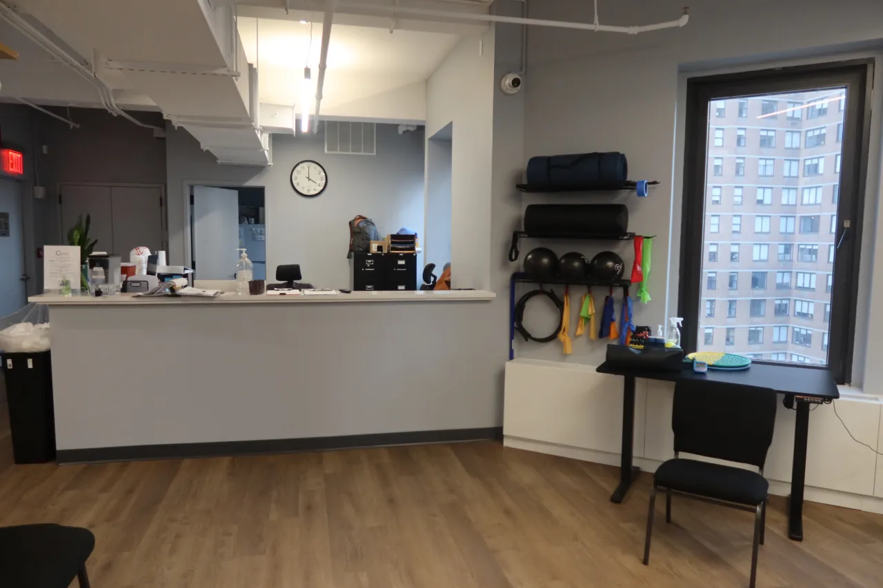Front desk with a wall rack of medicine balls, rollers and resistance bands beside the window