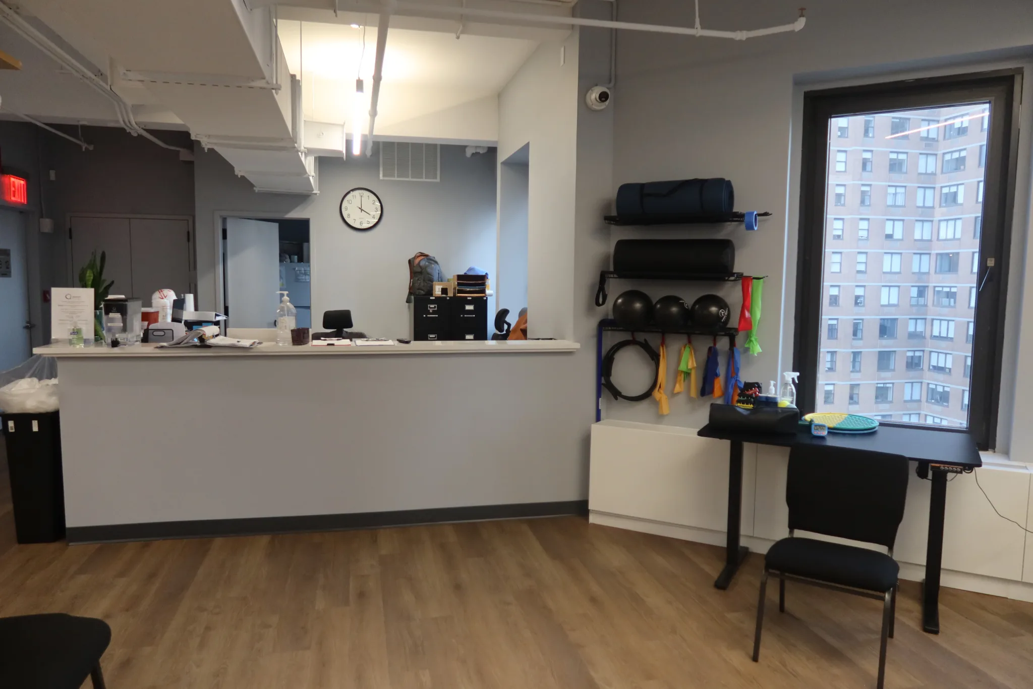 Front desk with a wall rack of medicine balls, rollers and resistance bands beside the window