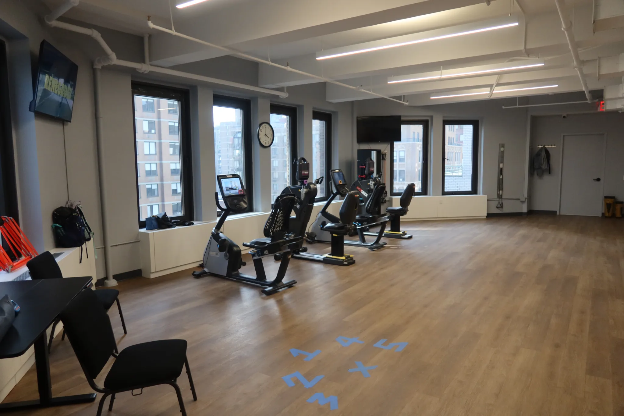 Open exercise floor with cardio machines along the windows and a view over Midtown Manhattan