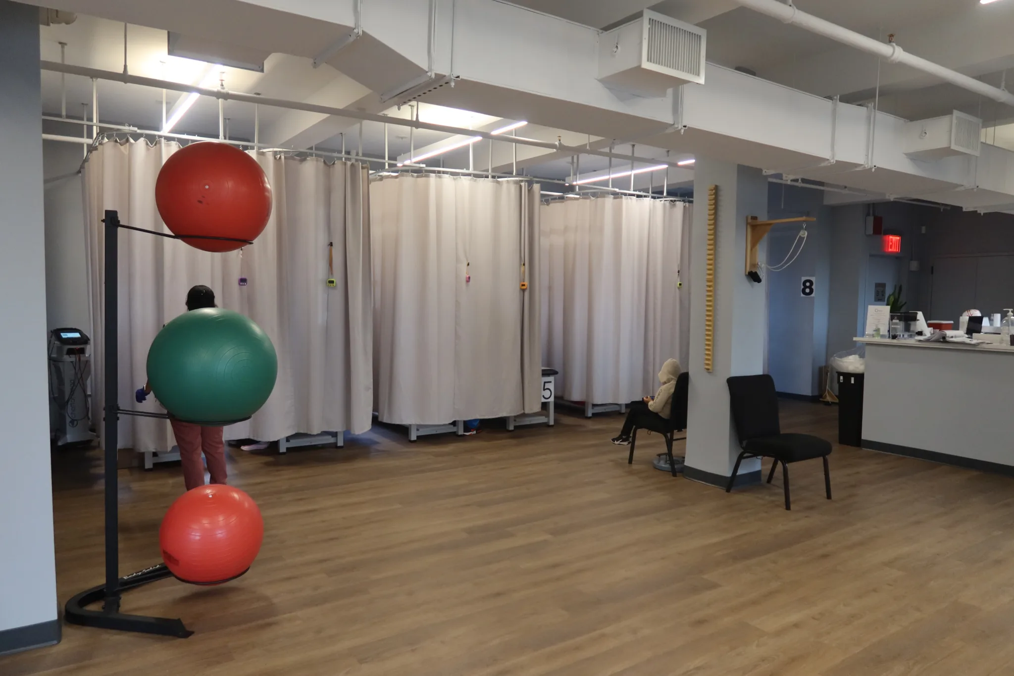 Curtained treatment bays with numbered stations and a rack of exercise balls in the foreground