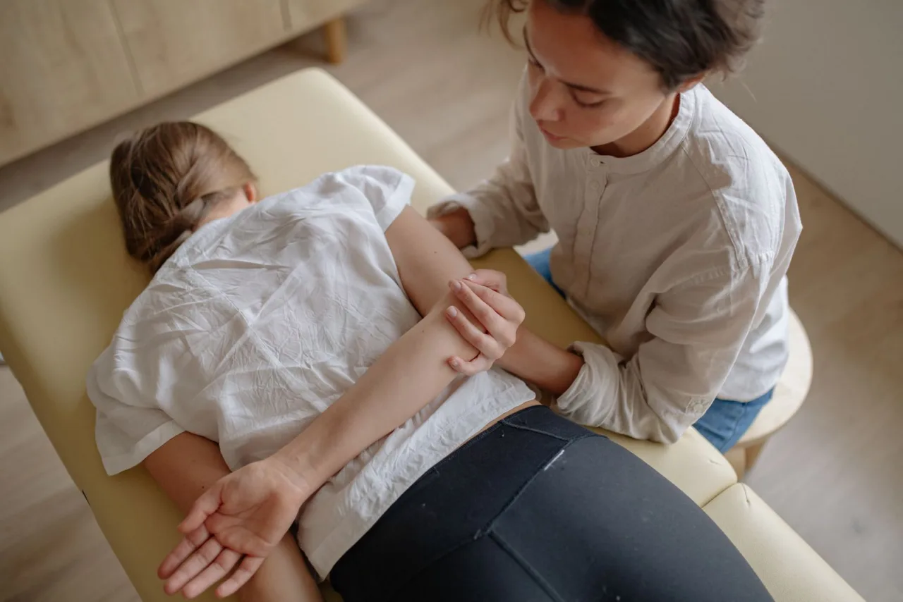 A chiropractor adjusts the arm and shoulder of a patient lying on a treatment table.
