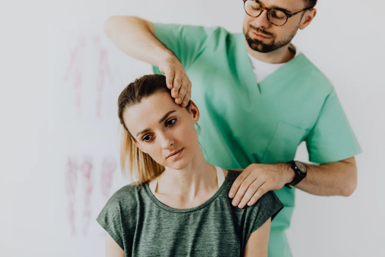 A chiropractor examines the neck of a seated patient, one hand at the base of the skull.