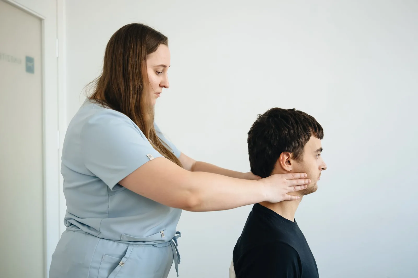 A chiropractor supports a seated patient's neck during an examination.