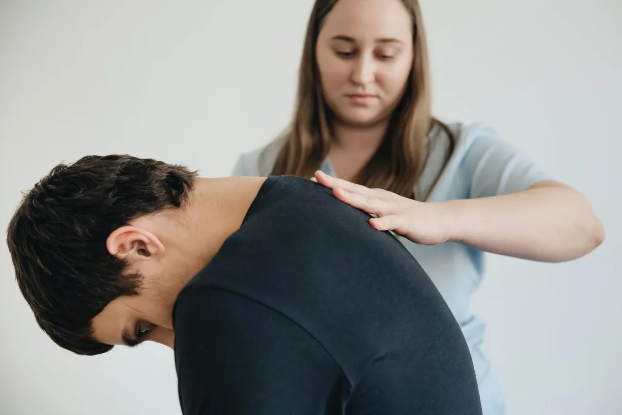 A practitioner treats the neck and shoulders of a patient leaning forward.